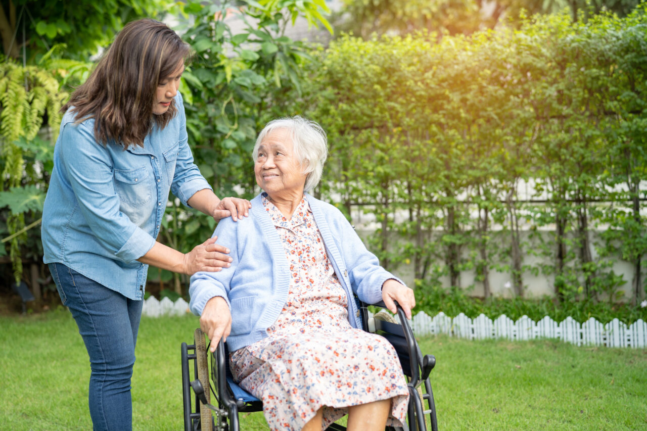 048f397ec0fc3325d3423a21e03c3c60f6392a90 A carer walking with a resident through the garden of an aged care home
